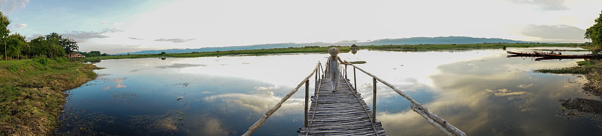 Young woman standing on wooden bridge above lake at sunset. People travel solo and like locals concept.