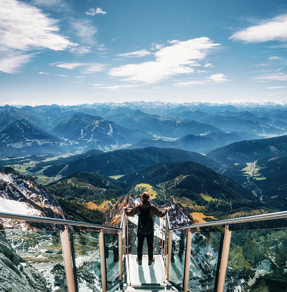 Young man with backpack stands on observation deck of skywalk rope bridge Dachstein Mountains and enjoys the landscape in Austria