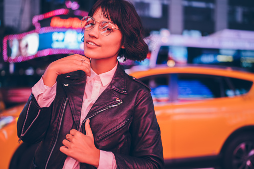 Attractive hipster girl in stylish apparel posing on urban setting background enjoying leisure, portrait of beautiful young woman dressed in leather jacket looking at camera standing on publicity area