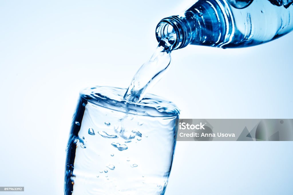 Fresh drinking water is poured in a glass Fresh drinking water is poured in a glass. Blue background. Water Stock Photo