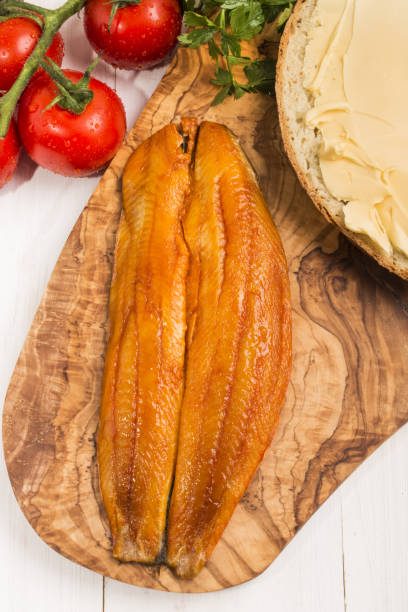 Cтоковое фото копченая филе киппера, кусок хлеба с маслом, помидоры и петрушка на деревянной доске