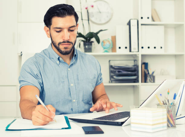 istock Young male is reading documents and looking in laptop 897969326