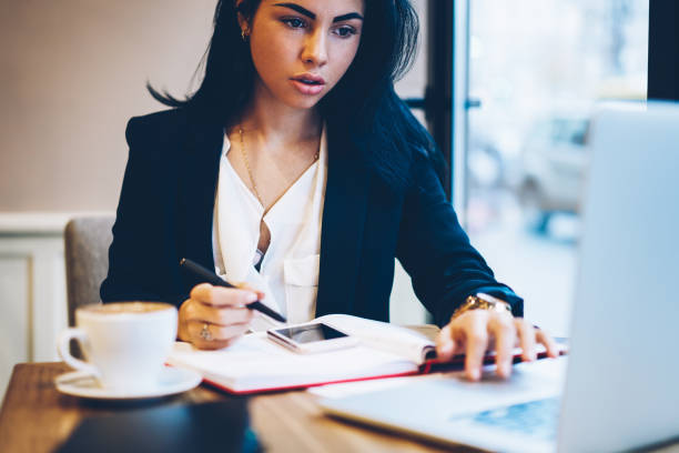 istock Cropped image of beautiful graphic designer watching training webinar on laptop computer and writing down general concepts.Young pretty businesswoman transferring money online and recording balance 897969570
