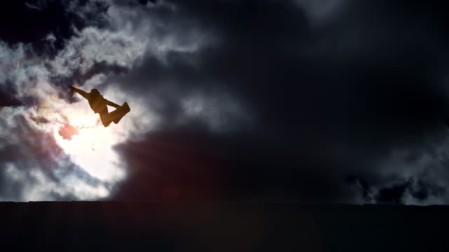 SLO MO Freestyle snowboarder jumping in the half-pipe with clouds in the background