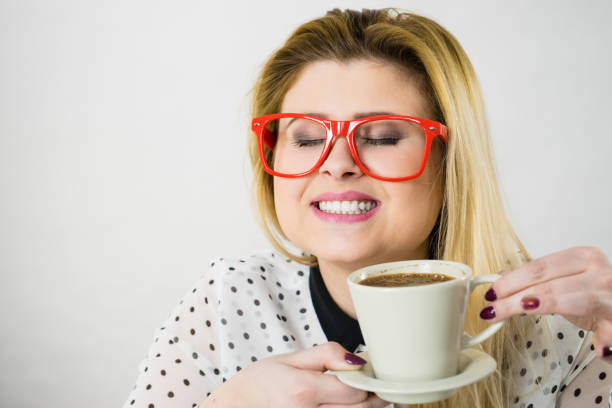 Happy young woman wearing eyeglasses at office drinking hot coffee or tea enjoying her break time during work. Job relax.