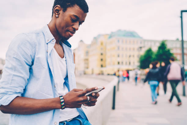 istock Cropped image of pondering hipster guy sending messages via application on cellphone during summer walk at street.Young handsome male traveler spending free time outdoors and texting feedback on phone 897982496