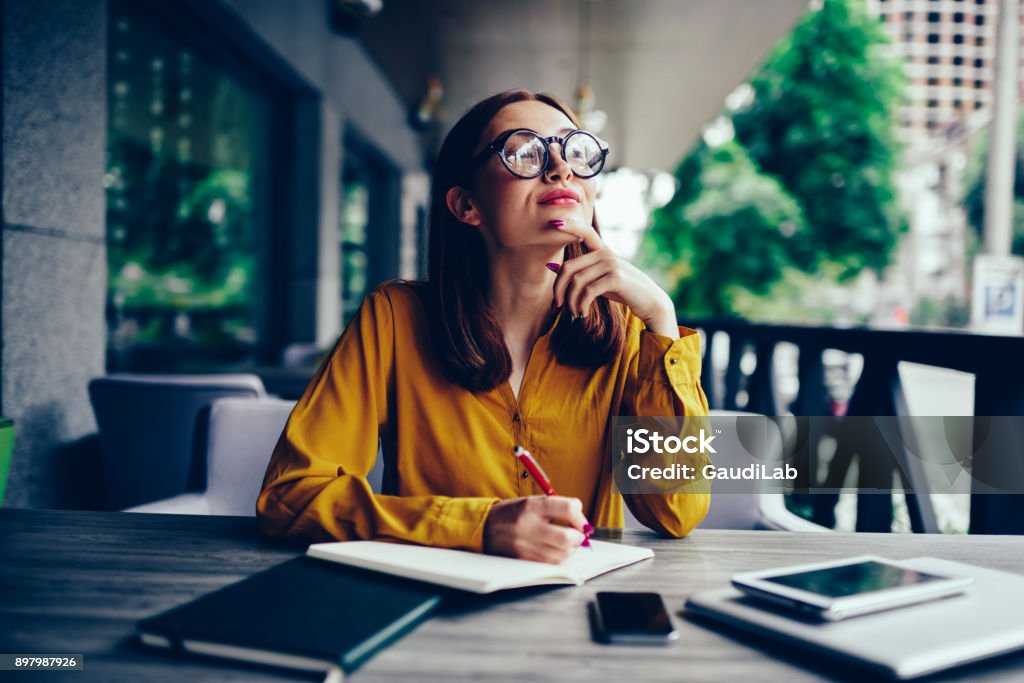 Grübeln Sie süße talentierte Studentin in coole Brille wegschauen und denken während der Vorbereitung für die bevorstehenden Prüfungen. Nachdenklich charmante Rothaarige Hipster Mädchen aufzuschreiben, Informationen zum Notizblock im café - Lizenzfrei Gelb Stock-Foto