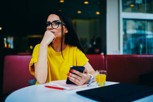 istock Contemplative beautiful female blogger in eyewear thinking about creative ideas for publication in personal website.Young cute hipster girl spending leisure time in coffee shop with modern gadget 897992156