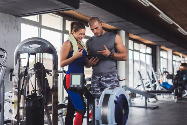 istock Young woman discussing workout progress with fitness instructor 897998770