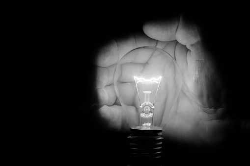 Human hand holding a light bulb to conserve energy in darkness artistic conversion