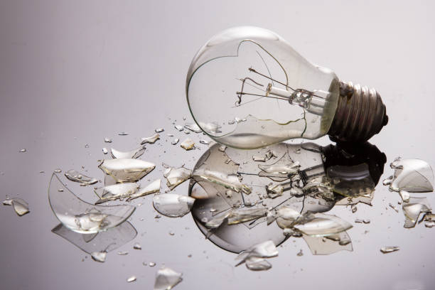 Broken light bulb on shiny surface with pieces backlit stock photo