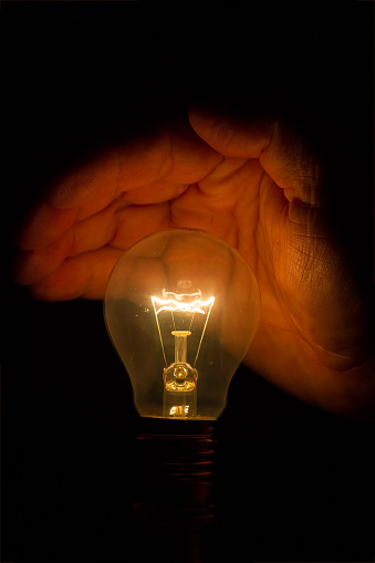Human hand holding a light bulb to conserve energy in darkness