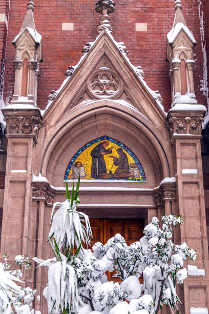 Budapest, Hungary, April 2025The facade of the Pest Franciscan Church.The upper facade of a Baroque-style church features detailed white and pale yellow stucco architecture with sculpted statues of religious figures, including a saint with a crosier and another with a sword, positioned on pedestals. A prominent cross rises from the roofline, flanked by ornate urns and a radiant sunburst motif. Below, a niche contains a relief sculpture of the crucifixion scene with Jesus on the cross. The structure includes arched windows and decorative scrolls, set against a cloudy gray sky during daytime. No people are present. This image captures the grandeur of historic religious architecture in Europe, suitable for commercial use in travel magazines, architectural books, historical documentaries, religious publications, and tourism promotions highlighting cultural heritage sites.