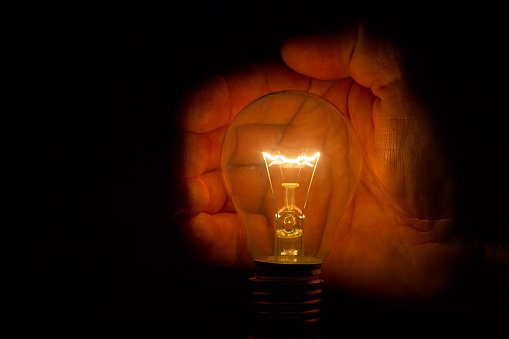 Human hand holding a light bulb to conserve energy in darkness