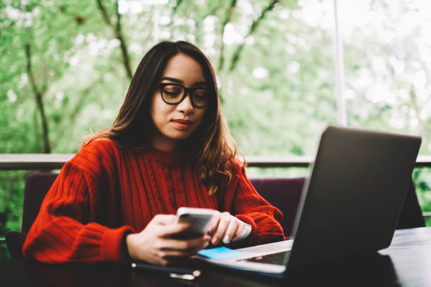 istock Pensive young woman checking email on smartphone and sending feedback working remotely in cafe, female student downloading files on mobile phone sitting with laptop computer for searching information 898009706