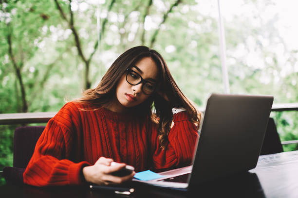 istock Pensive female freelancer reading information making researches for online project spending time in cafe, young woman waiting for confirmation message on mobile for log in banking account on web page 898009782