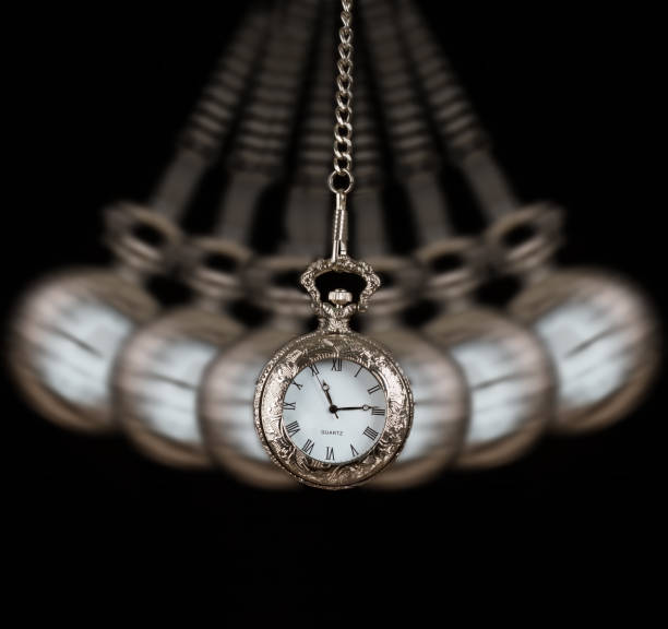Pocket watch silver swinging on a chain black background to hypnotize stock photo