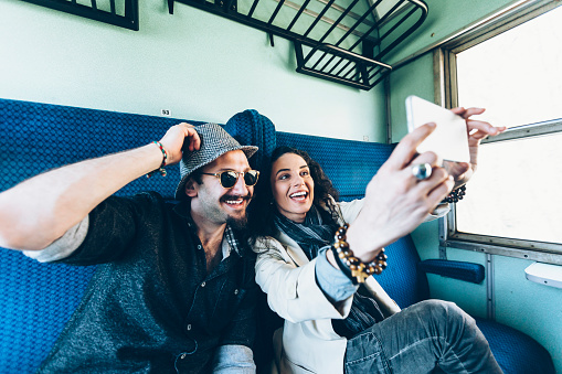 Cheerful couple tourists traveling with train and taking selfie. Both with casual clothes, man with hat and sunglasses.