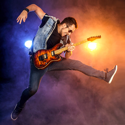 Young guitarist jumping with a guitar on stage. About 25 years old, Caucasian male.