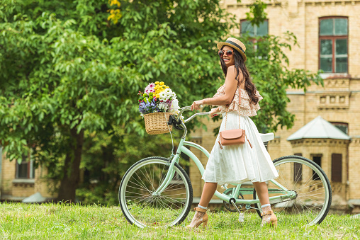 side view of beautiful smiling woman in vintage dress walking with bicycle in park
