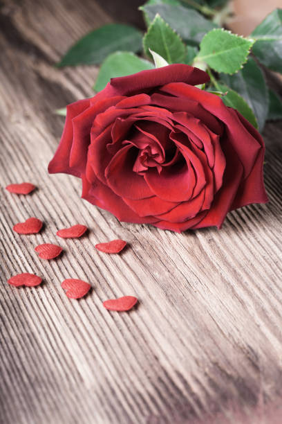 istock Single red rose witn small hearts on wooden background with copyspace 898057258