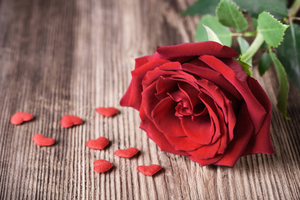 istock Single red rose witn small hearts on wooden background 898057264