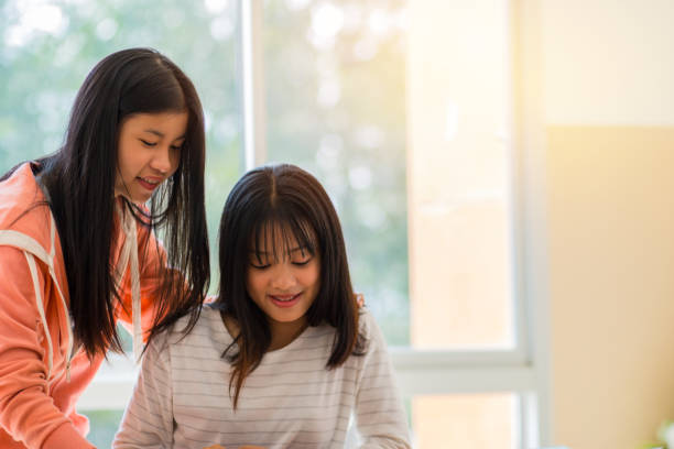 istock Asian University or college students studying together with tablet,laptop and documents paper for report near windows in classroom. Happy Asian young woman doing group study in Education class Concept 898063572