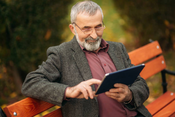 istock Grandpa use a tablet sitting in the pakr on the bench 898070346
