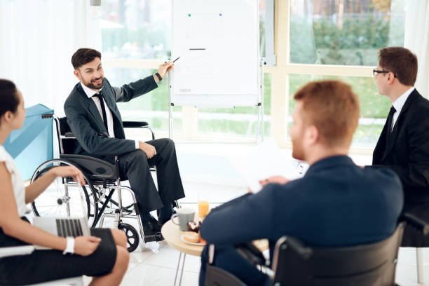 A man in a wheelchair is pointing at a graph on the blackboard.