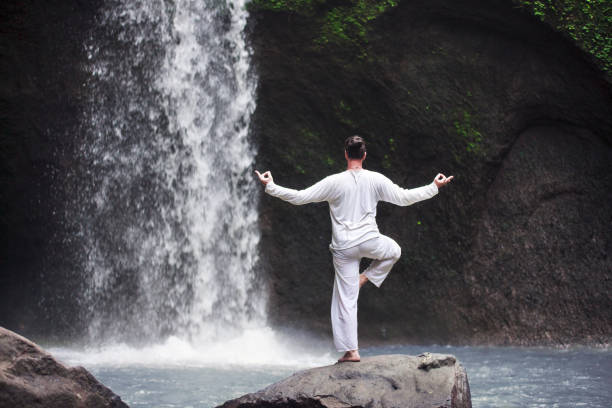 istock Man standing in meditation yoga on rock at waterfall 898095922