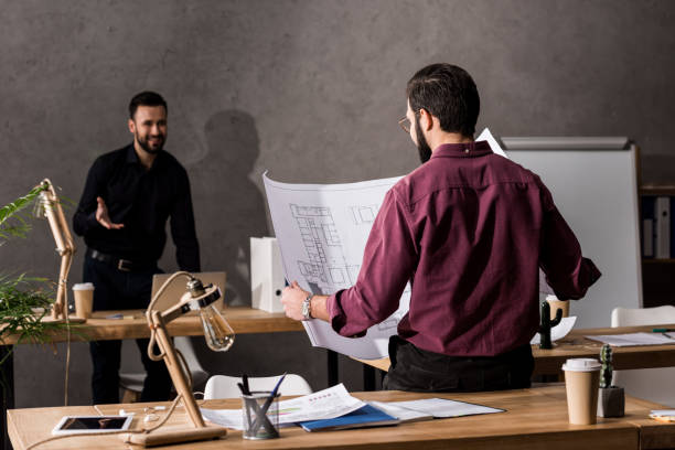 istock architect looking at blueprint in office and talking with colleague 898112178