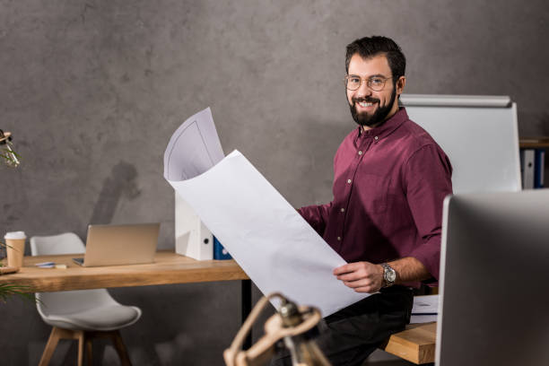 smiling architect holding blueprint and looking at camera stock photo
