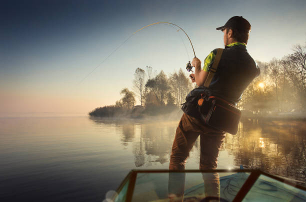 pesca. hombre pescando en un lago en barco - fishing reel fotografías e imágenes de stock