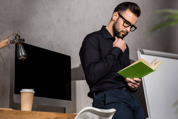 istock thoughtful businessman standing and reading book in office 898140812