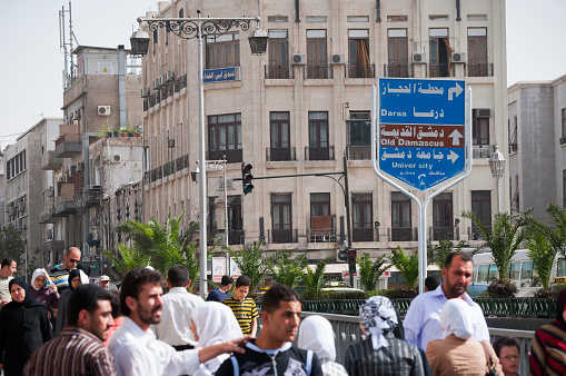 Pedestrians walk in central Damascus past a sign giving directions to the city of Daraa, as well as to the old city and university in Damascus.