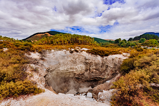 A large hole in the ground reveals the view of earth with different chemical porperties at the Whakarewarewa park witch is a geothermal area within Rotorua city in the Taupo Volcanic Zone of New Zealand.