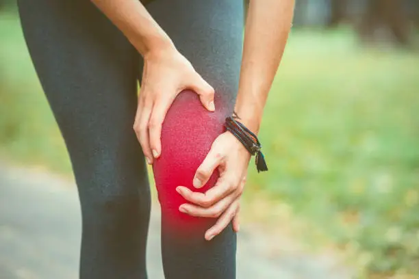 Woman holding her knee with red painful during a workout session sport. Pain relief concept