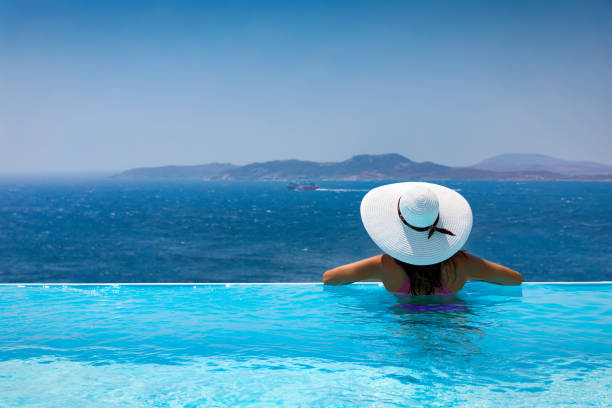 Attractive woman  enjoys the view from the pool to the Mediterranean sea Attractive woman with beautiful hat enjoys the view from the pool to the Mediterranean sea during summer infinity pool stock pictures, royalty-free photos & images