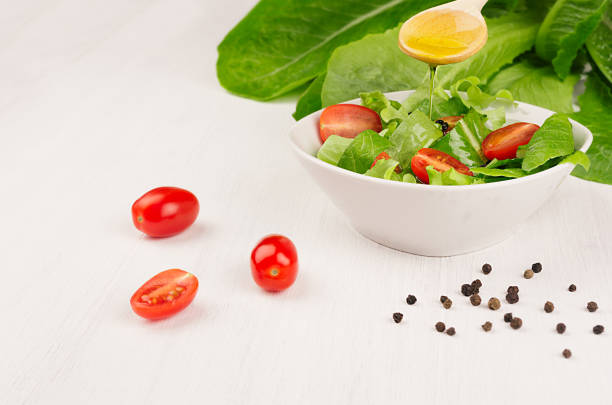 dieting raw healthy food - fresh green salad with tomatoes, pepper and olive oil on soft white wood board, closeup, copy space. - cooking oil olive oil nutritional supplement spoon imagens e fotografias de stock