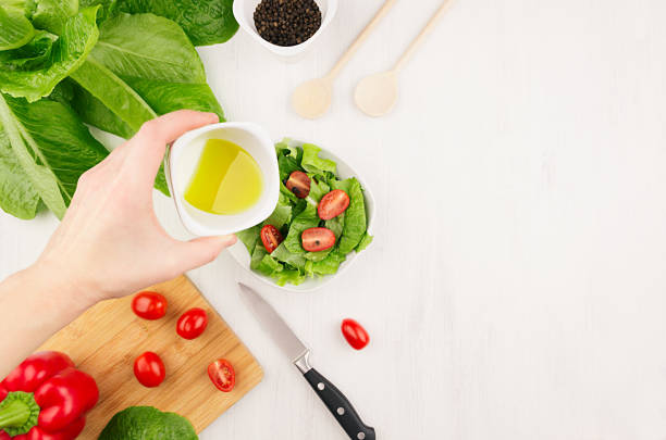 cooking dieting raw healthy salad - olive oil  flow down on fresh green salad with tomatoes in bowl, ingredients on soft white wood board, copy space. - cooking oil olive oil nutritional supplement spoon imagens e fotografias de stock