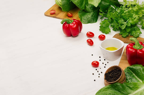 Raw fresh green vegetables, greens, red cherry tomatoes and kitchenware on soft white wood board, border. Spring vitamin dieting food.