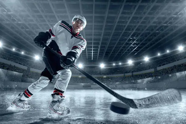 Ice hockey players on big professional ice arena with hockey stick. The player scores a goal. Hockey puck flies into the camera. Player dressed in a non-branded sports ice hockey uniform.