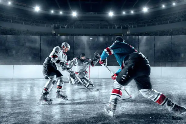 Ice hockey players on big professional ice arena. Goalkeeper protects the goal. Opponent scores a hockey puck in the goal. Two teams dressed in a non-branded sports ice hockey uniform.