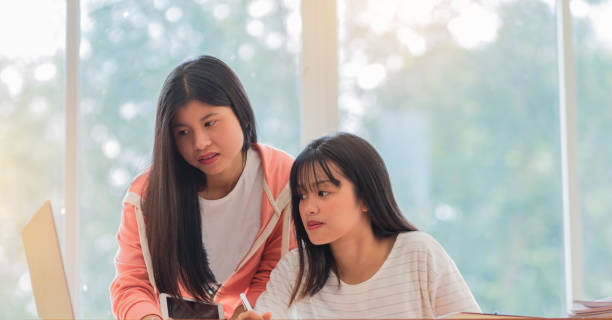 istock Asian University or college students studying together with tablet, laptop and documents paper for report near windows in library. Happy Asian young woman doing group study in Education Concept. 898232774