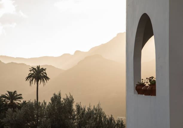 Arch window with plants, and palm trees and misty mountains in the background. Santa Lucia, Gran Canaria in Spain.