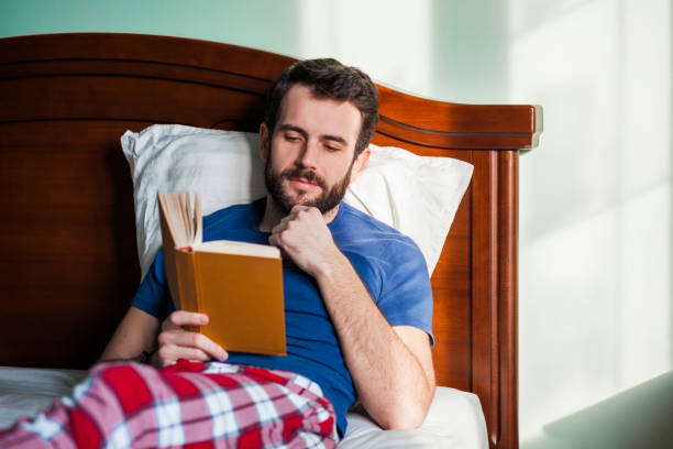 istock Young man reading a book in his bedroom 898238022