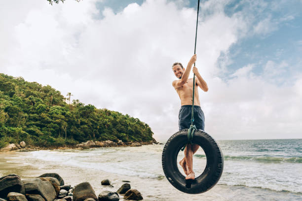 reifenschaukel am tropischen strand - men swing rope swing tire stock-fotos und bilder