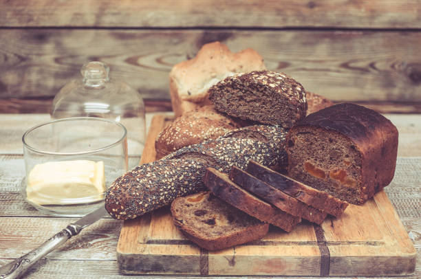 Various of wheat and rye bread on a chopping board. Bread, table knife and butter. Healthy breakfast concept. Easy toning. Wooden background