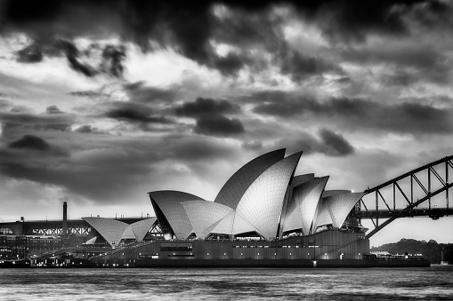 Sydney: Magical sunset over world famous landmark - Sydney Opera house and Harbour Bridge. Side view of illuminated opera in black-white.