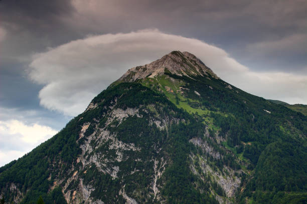 Lens shaped cloud above sharp green forested Polinik peak, Plocken Pass, Carnic Alps Main Ridge, Carinthia, Austria, Europe